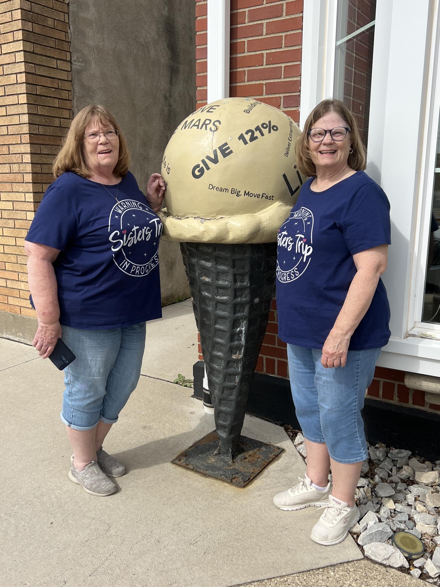 Two sisters visiting Le Mars, Iowa, pose beside a downtown ice cream cone sculpture outside the CENTURY 21 ProLink office during their sisters’ weekend trip.
